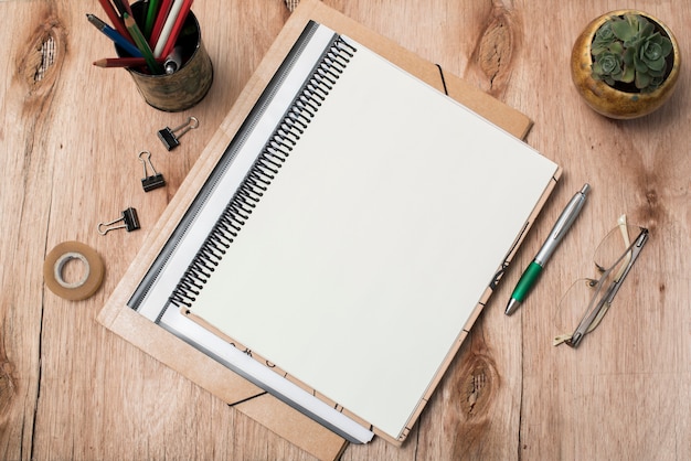 Free photo top view of blank spiral book; eye glasses; plant and office supplies on table