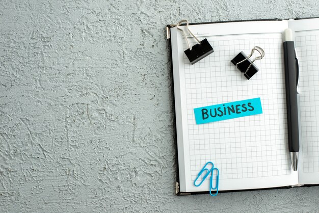 Top view of blue color business pen and open spiral notebook on gray sand background