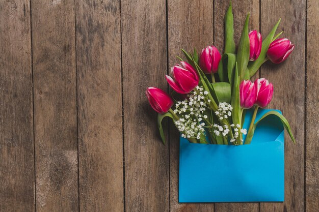 Top view of blue envelope with flowers on wooden table