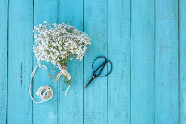 Top view of blue wooden surface with flowers and scissors