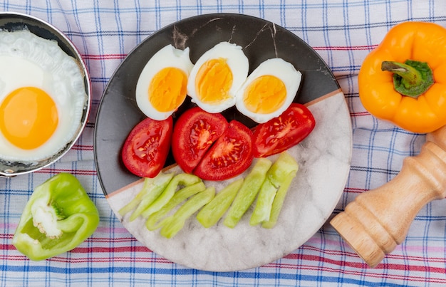 Free photo top view of boiled halved eggs on a plate with chopped slices of tomatoes and green bell peppers on a checked tablecloth background