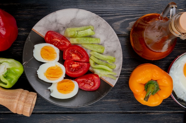 Top view of boiled halved eggs on a plate with peppers with apple vinegar on a wooden background