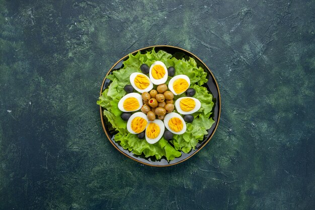 top view boiled sliced eggs with olives and green salad on dark background