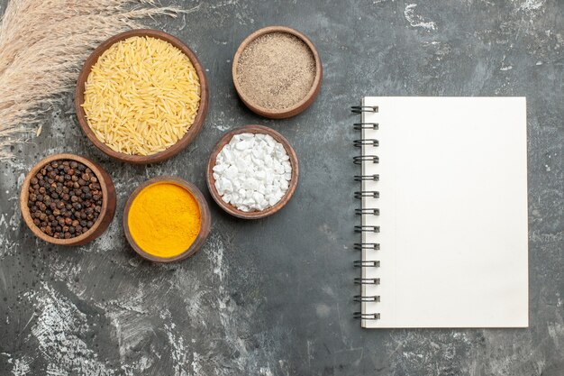 Top view of boiled and uncooked white rice and different spices next to notebook