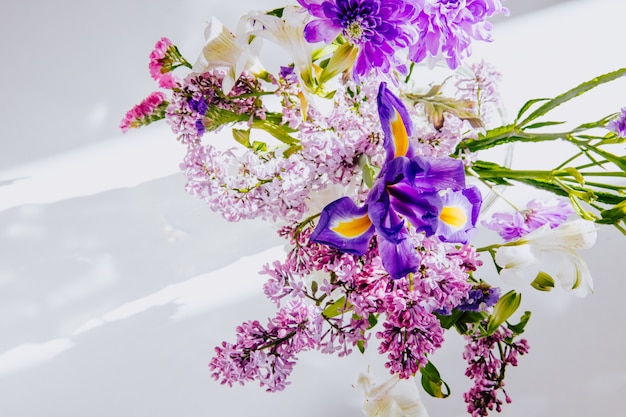 Top view of a bouquet of lilac flowers with white color alstroemeria dark purple iris and statice flowers in a glass vase on white background