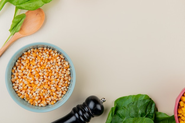 Top view of bowl of corn seeds with spinach and wooden spoon on white with copy space