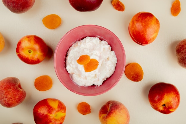 Free photo top view of bowl of cottage cheese with raisins and peaches around on white surface