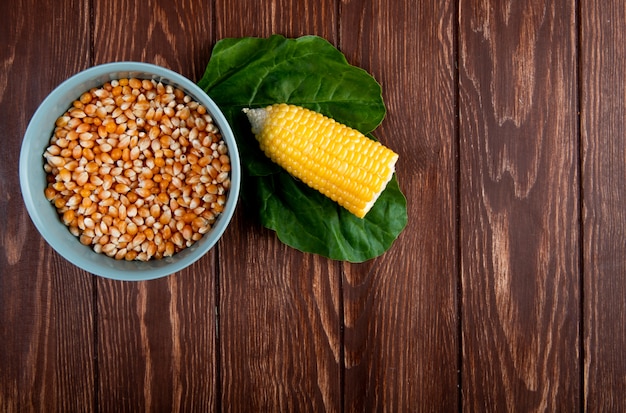 Top view of bowl full of dried corn kernel with cut cooked corn and spinach on wood with copy space