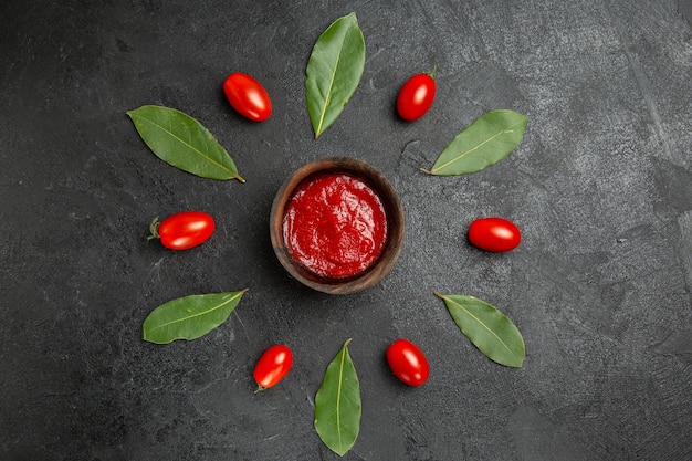 Free photo top view a bowl of ketchup around cherry tomatoes and bay leaves on dark ground