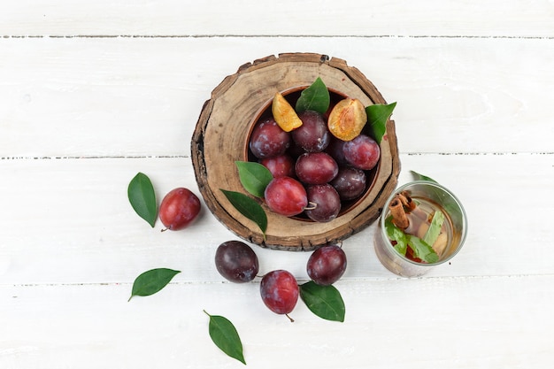 Free Photo top view a bowl of plums on wooden board with detox water and leaves on white wooden board table. horizontal