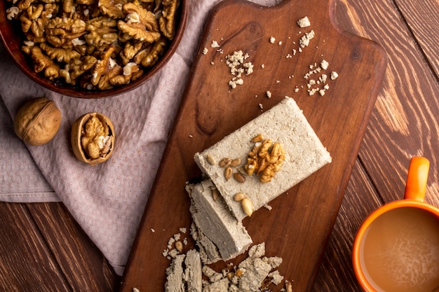 Top view of a bowl with walnuts and sweet halva slices on a wooden board