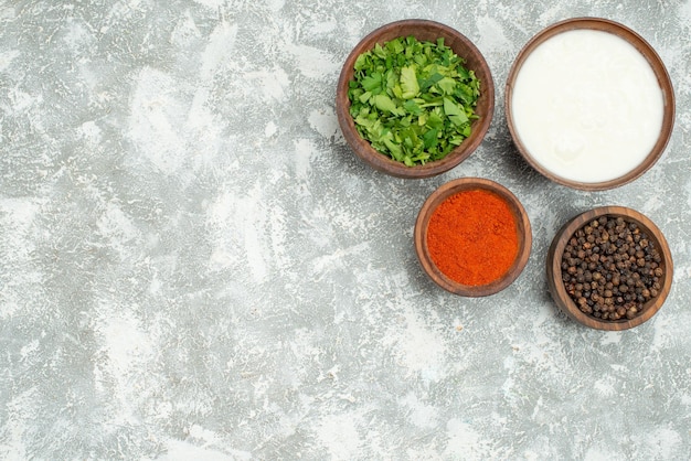 Free photo top view bowls of spices bowls of spices black pepper herbs and sour cream on the right side of grey table