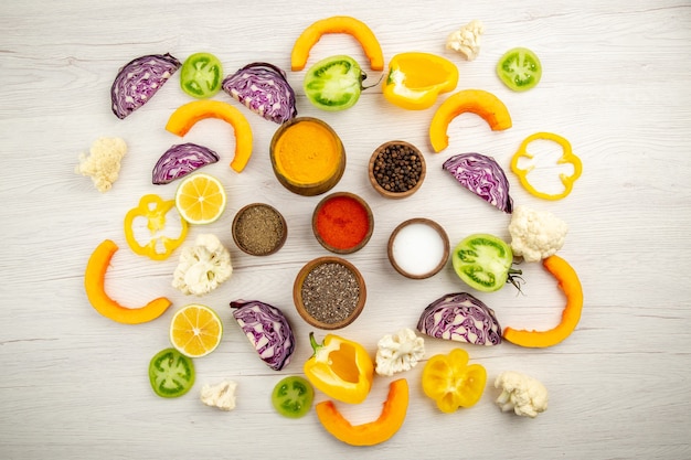 Top view bowls with spices turmeric black pepper salt red pepper powder cut vegetables on white surface