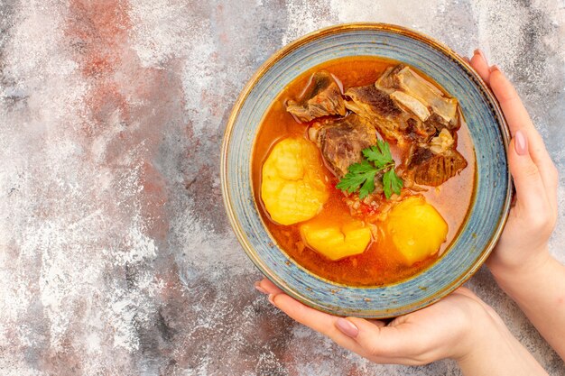 Free photo top view bozbash soup in a bowl in female hand on nude background