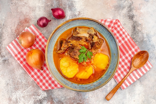 Top view bozbash soup kitchen towel a wooden spoon yellow and red onions on nude background