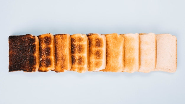 Free photo top view of bread slices at varying stages of toasting arranged in row on white background