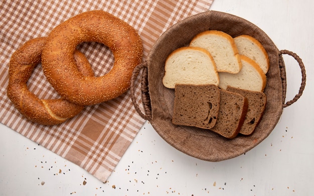 Top view of breads as turkish bagel on cloth and basket with white and rye bread slices on white background