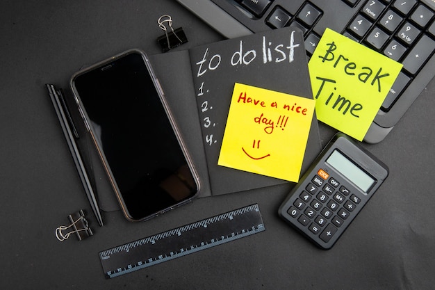 Free Photo top view break time and have a nice day written on sticky notes to do list on black notepad phone pen calculator ruler binder clips keyboard on black table