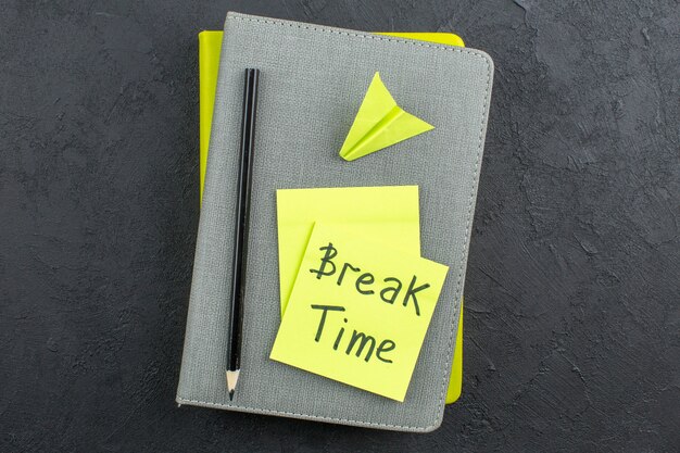 Top view break time written on yellow sticky notes black pencil on colorful notepads on dark table