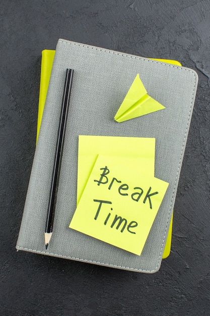 Free photo top view break time written on yellow sticky notes paper plane black pencil on notepads on dark table