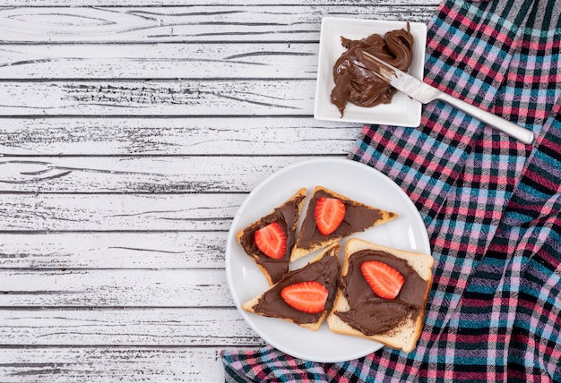 Free Photo top view of breakfast toasts with chocolate and strawberry with copy space on white wooden background horizontal