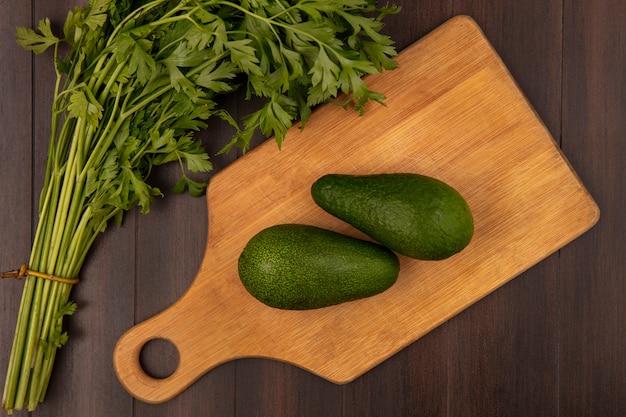 Top view of bright green avocados on a wooden kitchen board with parsley isolated on a wooden wall