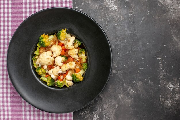 Top view broccoli and cauliflower salad on black oval plate on serving tray pink and white checkered tablecloth on dark surface free space