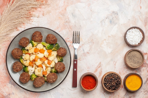 Free photo top view broccoli and cauliflower salad and meatball on plate bowls with colorful spices a fork on nude background with copy space