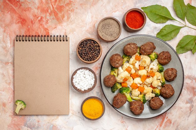 Free Photo top view broccoli and cauliflower salad and meatball on plate different spices in small bowls a notebook on nude isolated background