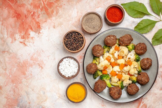 Top view broccoli and cauliflower salad and meatball on plate different spices in small bowls on nude isolated background free place