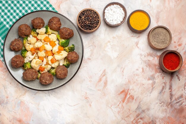 Top view broccoli and cauliflower salad and meatball on plate green and white checkered napkin colorful spices in small bowls on nude isolated background free place