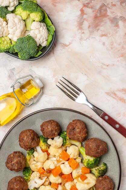 Top view broccoli and cauliflower salad and meatball on plate green and white checkered napkin a fork oil bottle raw vegetables on plate on nude isolated background