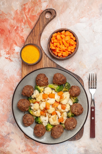 Free Photo top view broccoli and cauliflower salad and meatball on plate and turmeric on cutting board a fork cutting carrot in bowl on nude isolated background