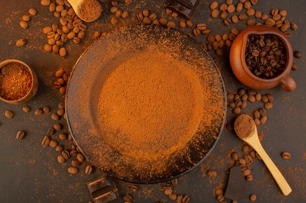 A top view brown coffee seeds along with black plate full of coffee powder with choco bars all over the the brown background