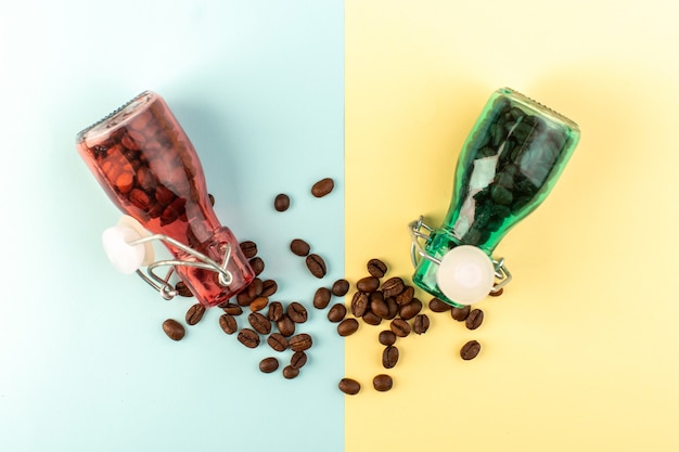 A top view brown coffee seeds inside colored glass jars on the blue-yellow surface coffee seed drink color photo