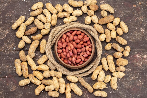 Top view brown raw nuts inside round bowl with ropes and yellow nuts on brown, nut walnut snack salt