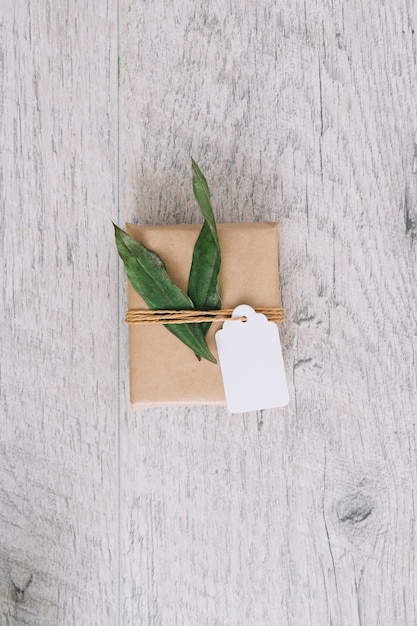 Free Photo top view of brown wrapped gift box with tag and green leaves on wooden table