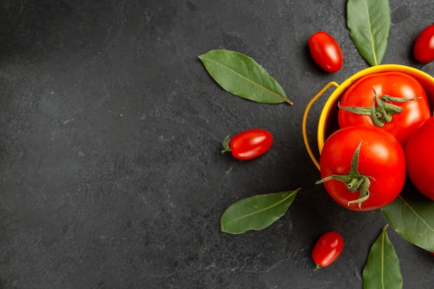 Top view a bucket with tomatoes around cherry tomatoes and bay leaves on the right of dark ground