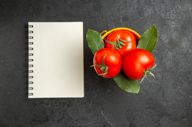 Free photo top view a bucket with tomatoes and bay leaves and a notebook on dark ground