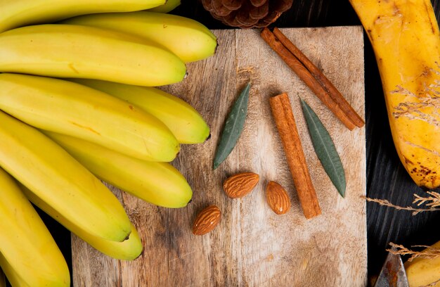 Top view of a bunch of banana with almond and cinnamon sticks on a wooden board