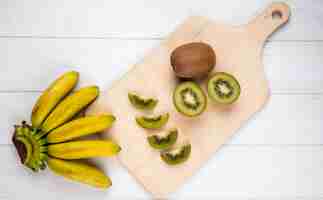 Free photo top view of bunch of banana with slices of kiwi fruit on wooden cutting board on white rustic