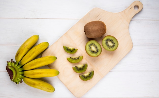 Free Photo top view of bunch of banana with slices of kiwi fruit on wooden cutting board on white rustic