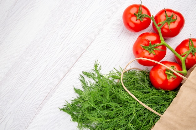 Top view of a bundle of green onion in a basket and tomatoes with stem on the left side on white background