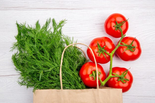 Top view of a bundle of green onion in a basket and tomatoes with stem on white background