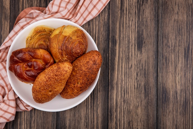 Top view of buns on a plate on a checked cloth on a wooden background with copy space