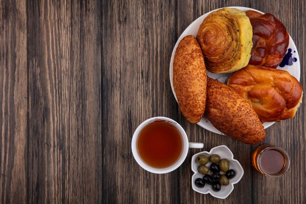 Top view of buns on a plate with a cup of tea with olives on a bowl and honey on a wooden background with copy space