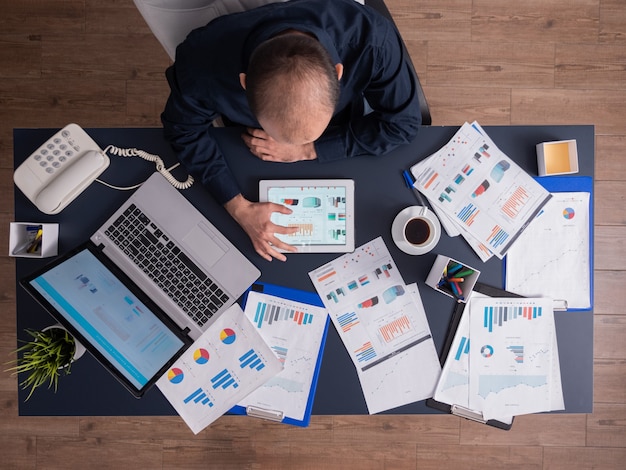 Free photo top view of businessman using tablet pc analyzing financial charts and documents, sitting at desk in corporate office