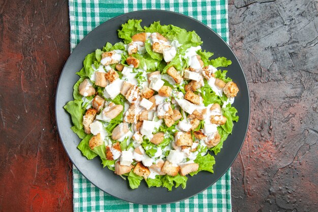 Top view caesar salad on oval plate green white checkered tablecloth on dark red background