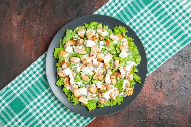 Top view caesar salad on oval plate green white checkered tablecloth on dark table