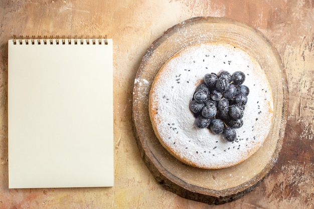 Top view of cake a cake with black grapes on the cutting board white notebook